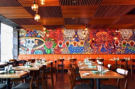 Modern Mexican restaurant interior featuring vibrant Day of the Dead mural artwork, orange booth seating, and wooden tables with contemporary chairs