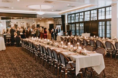 Luxurious wedding reception setup with French bistro chairs, candlelit long tables, and elegant table settings in a sophisticated banquet venue space