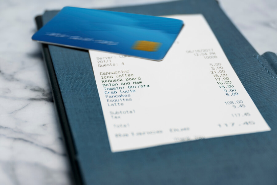 Close-up of a restaurant receipt and credit card, highlighting itemized charges and total cost as part of POS system transaction