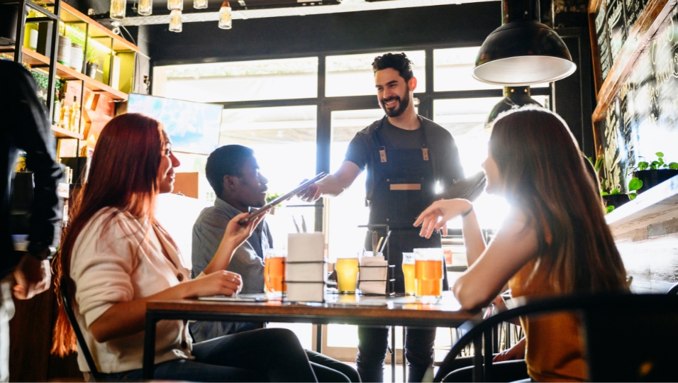 Restaurant dining scene with server and guests — the cost of running a restaurant varies dramatically by state, driven primarily by whether servers must be paid full minimum wage regardless of tips