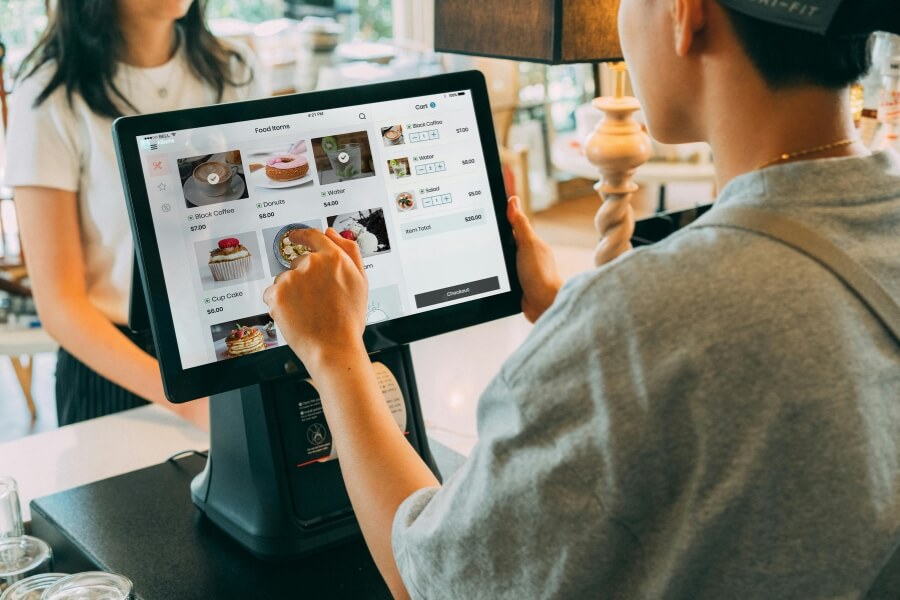 Restaurant staff using a modern POS touchscreen system to process customer orders at a cafe counter