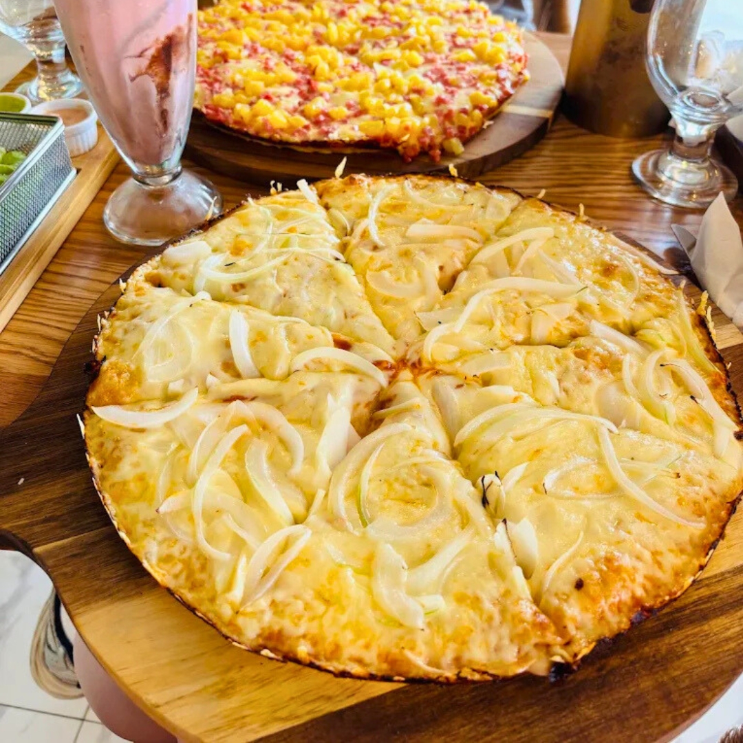 Cheese-and-onion pizza served on wooden paddle board atop handcrafted red-oak dining table inside La Juliana Miami.