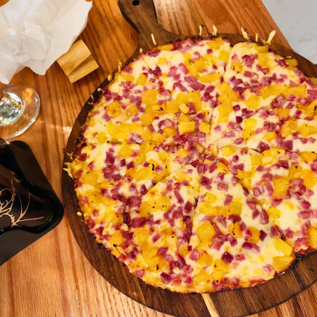 Thin-crust ham-and-pineapple pizza on rustic wood board over red-oak plank table—shareable entrée at La Juliana Miami.