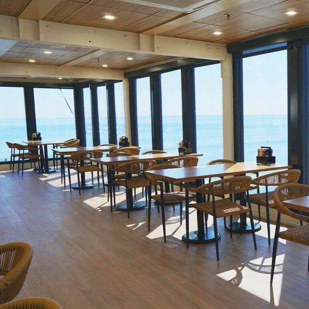 Pier 62's bright dining room in Cocoa Beach featuring natural rope chairs, wooden tables, and floor-to-ceiling windows with Atlantic Ocean views