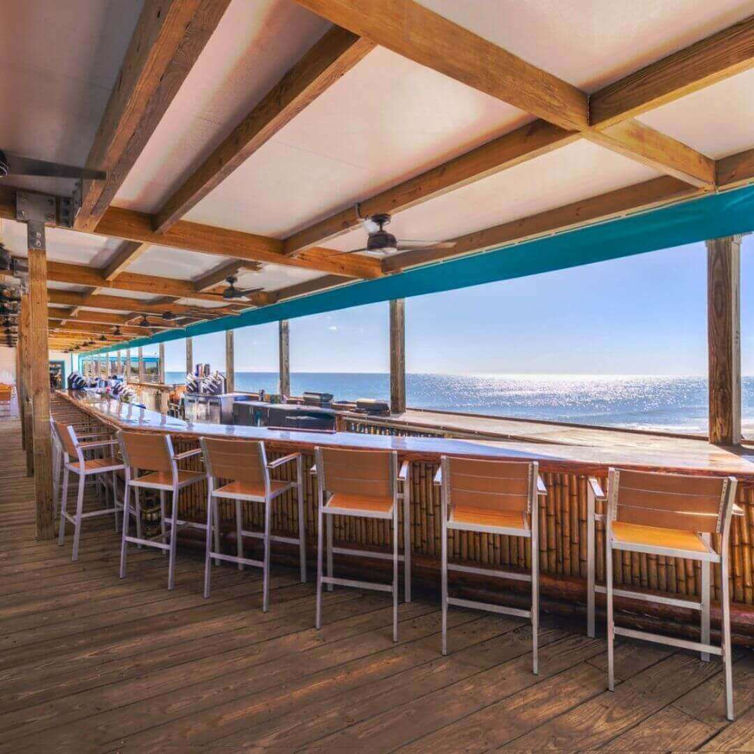 Oceanfront bar seating at Pier 62 Cocoa Beach with wooden deck, modern high chairs, and unobstructed views of the Atlantic