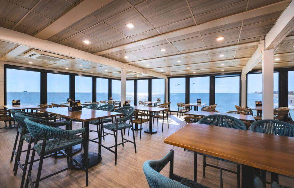 Pier 62's modern dining room in Cocoa Beach featuring floor-to-ceiling windows overlooking the Atlantic Ocean, with coastal-inspired turquoise chairs and wooden tables