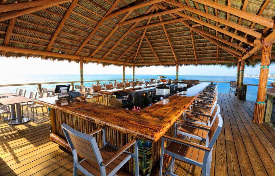 Rustic tiki bar at Pier 62 Cocoa Beach with custom wood countertops, teak wood outdoor bat stools, and panoramic oceanfront views from the covered deck